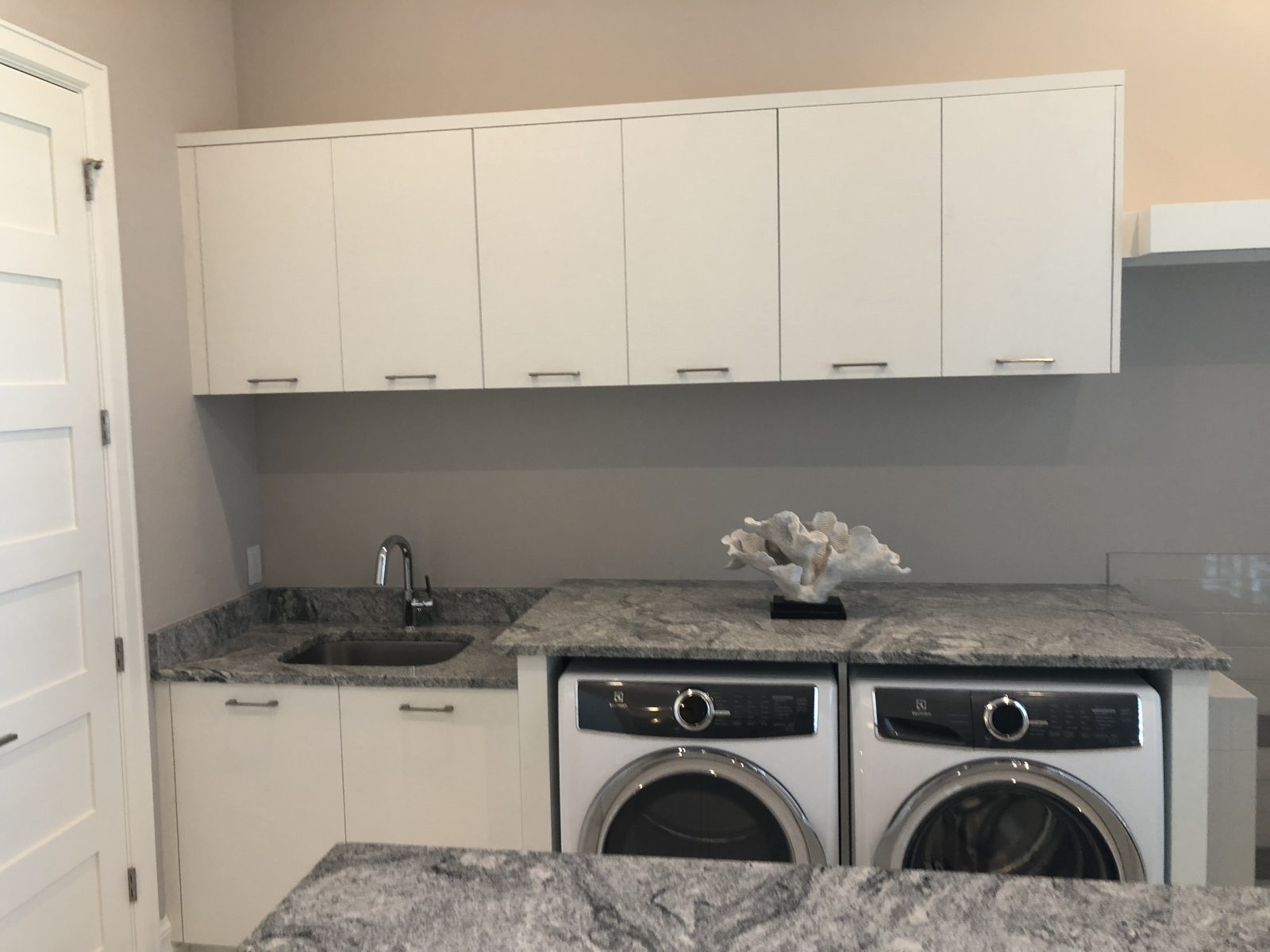Laundry room with white upper cabinets, granite counters and a utility sink