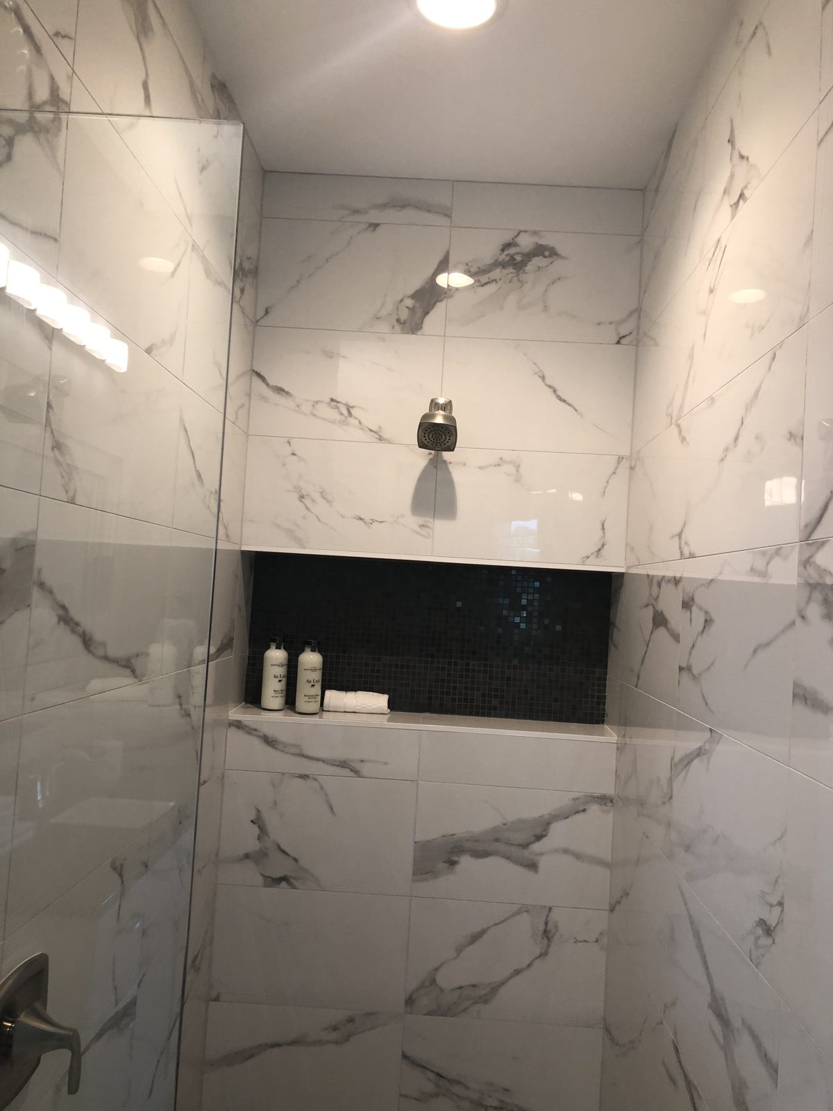 Walk-in marble-look tile shower with glass enclosure and recessed niche